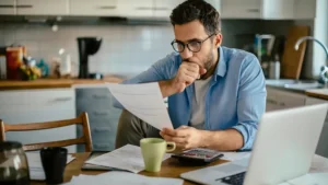 Worried young Caucasian man going over his bills and home finances in the morning in the kitchen